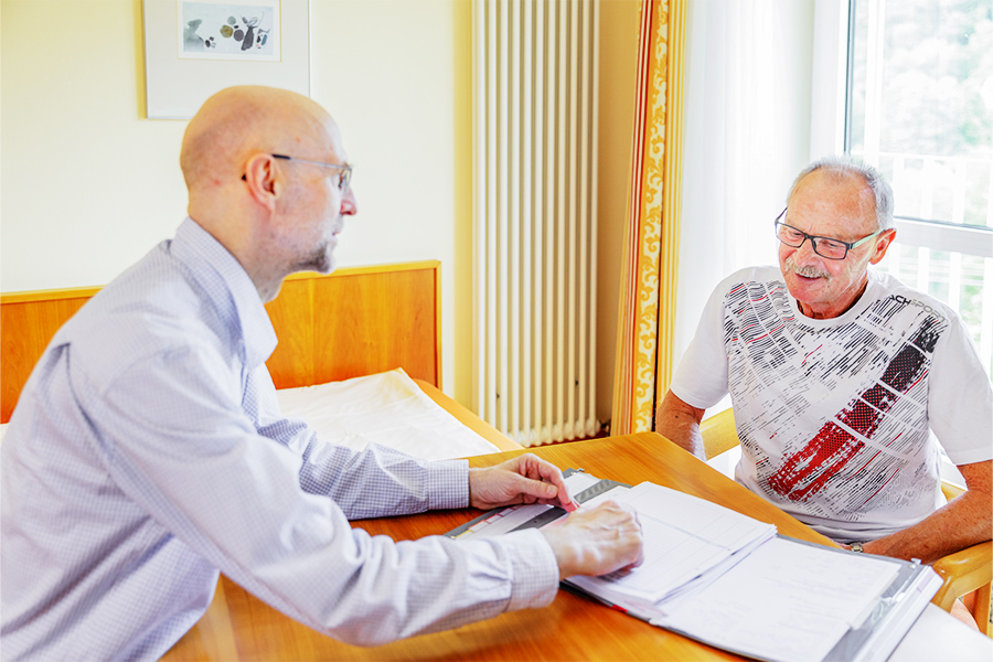 Ein Arzt und ein Patient sitzen sich an einem Tisch gegenüber und unterhalten sich über dessen Akte.