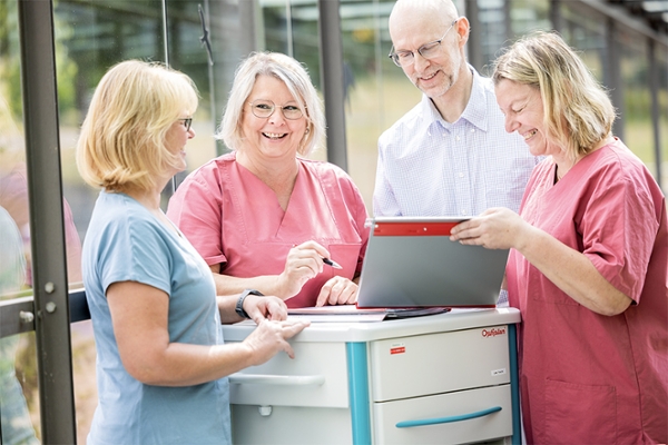 Vier Mitarbeitende einer Klinik stehen um einen Rollwagen und besprechen eine Patientenakte. Vier Mitarbeitende einer Klinik stehen um einen Rollwagen und besprechen eine Patientenakte.