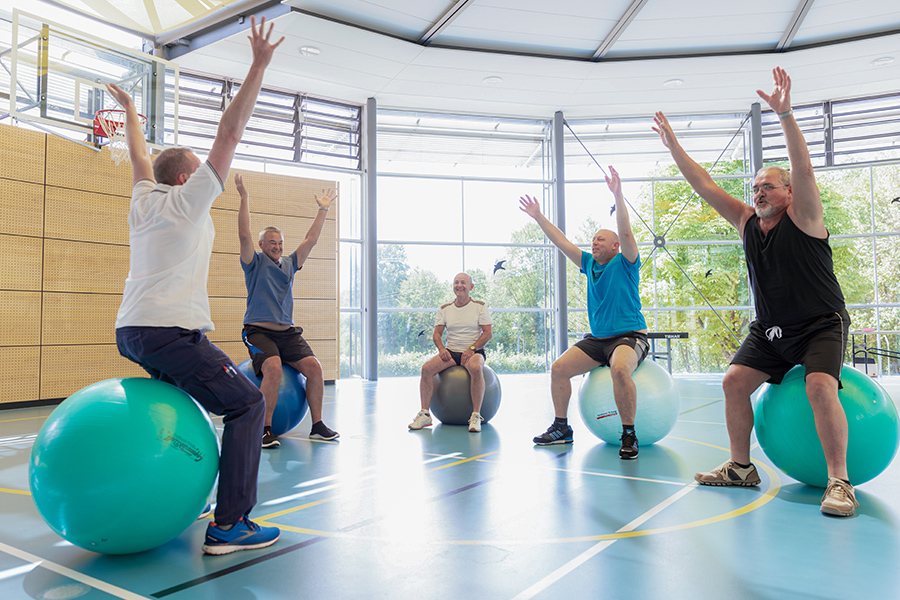 Ein Therapeut und mehrer Patienten machen Sportübungen auf Gymnastikbällen.