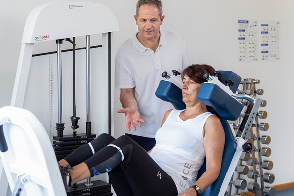 Ein Therapeut unterstützt eine Patientin beim Training an einer Beinpresse.